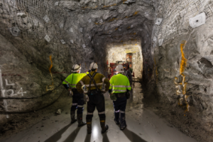 3 miners standing, survey the area of an underground mine.