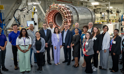 Acting Secretary Su and workers stand in front of heavy machinery at a manufacturing facility.