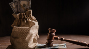 A sack of $100 bills sitting next to a judges gravel resting on top of a stack of $100 bills.