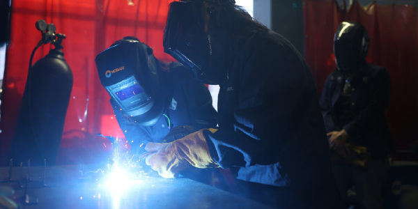 Acting Secretary Su, fully suited in protective gear, practices welding with assistance from two similarly attired welders.