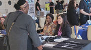 A female service member speaks with two transition assistance program representatives sitting at a booth at a job fair. 