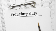 Eyeglasses placed above a white paper with black text reading âFiduciary dutyâ at the top with a ballpoint pen resting on the paper. 