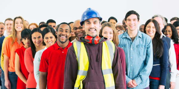 A man wearing a hardhat, ear protection and a high-visibility vest stands in front of a diverse group of smiling workers. 