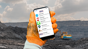 A miner’s gloved hand holds a mobile device that shows the Miner Safety + Health app menu. 