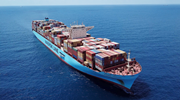 A Maersk mega container ship, fully loaded with stacks of freight containers, sails the dark blue Mediterranean Sea.