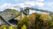 Mine conveyor belts rise above the treetops at a West Virginia mine. Wooded hills are visible in the distance.