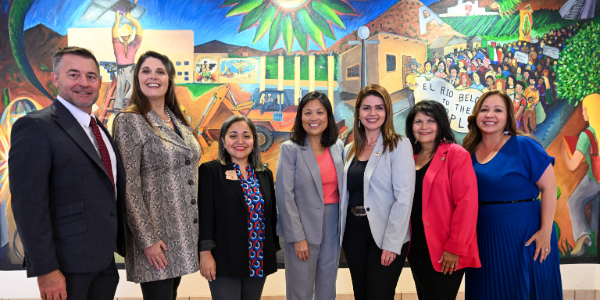 Acting Secretary Su poses for a photo with seven men and women in front of a colorful mural depicting workers.