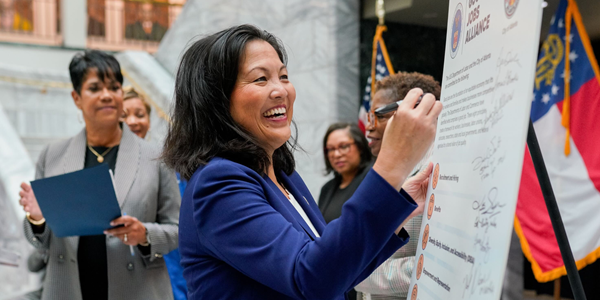 Acting Secretary Su smiles as she signs a poster outlining the Good Jobs Principles. Several local officials stand around her.