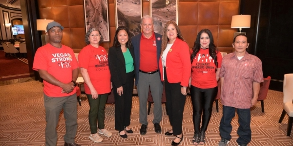 Acting Secretary Su stands in the middle of several union workers and leaders, who are all wearing red shirts.