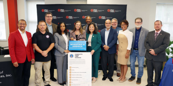 Acting Secretary Su poses for a photo with 11 professionally dressed people standing by signs that read âInvesting in Americaâ and outline the good jobs principles. 