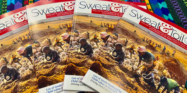 A pile of magazines spread out on a colorful blanket. The title is âSweat & Toilâ and the cover shows several children digging at an outdoor mine site.