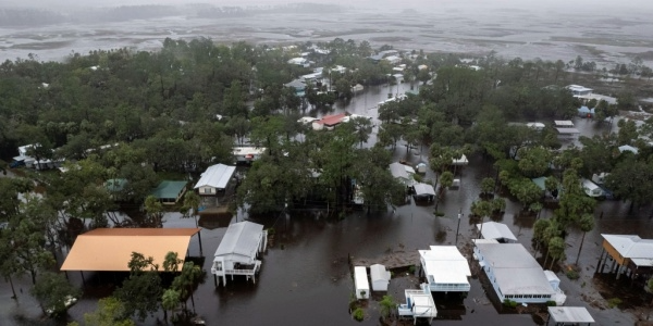 Aerial photograph of a hurricane-flooded neighborhood shows water surrounding houses (some on stilts) and wind-damaged trees 