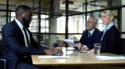 Black man looking across table at white male and female hiring executives. 