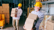 Two storage workers in work wear carrying heavy boxes.