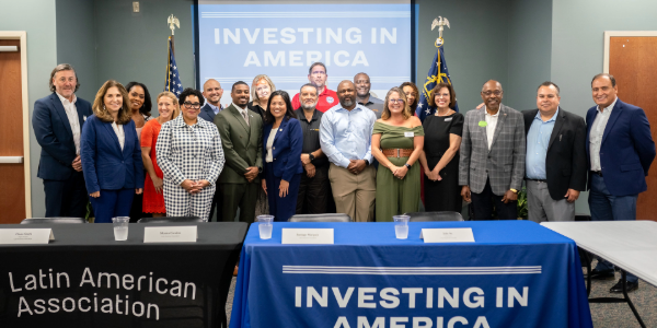 Acting Secretary Su poses with dozens of men and women in front of banners reading âLatin American Associationâ and âInvesting in America.â