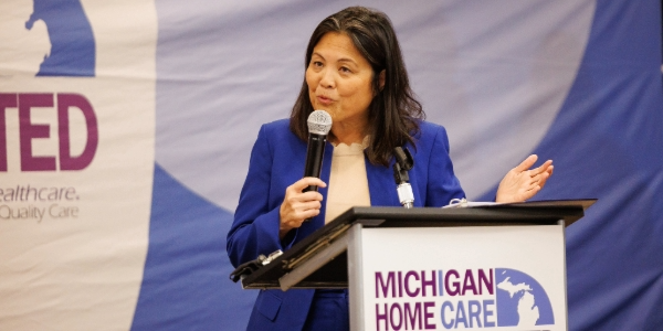 Acting Secretary Su speaks on a stage. The lectern in front of her has a sign reading Michigan Home Care Workers United.