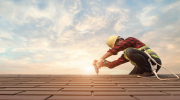 Roofer in yellow hard hat wears safety device while replacing shingles.