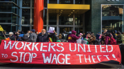 Protesting workers holding large red “Workers United to Stop Wage Theft” banner.