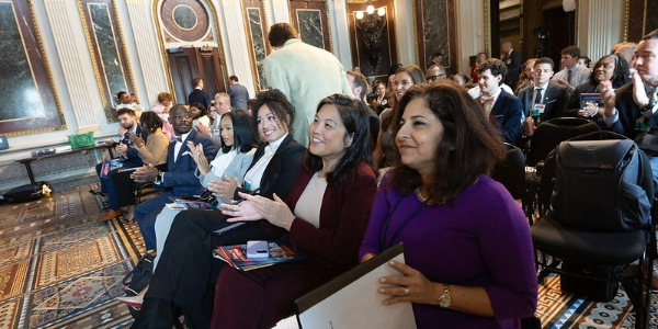 Acting Secretary Su applauds from the front row of an event in the White House’s Indian Treaty Room. The seats behind her are full of people in business attire.