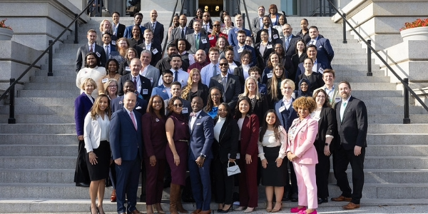 Dozens of people in business clothes and nametags pose, smiling, on the steps of a federal building.