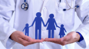 Blue paper cutout of a family with a mom, dad, daughter and son held in the hands of a medical professional wearing a white coat.