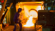 Male worker in protective gear removes melting iron in from a high temperature furnace.