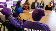 Acting Secretary Su at a table with a group of workers and local leaders, with some wearing purple