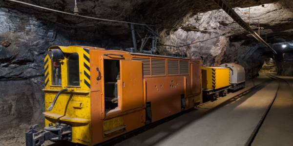 A yellow electric mining locomotive on a track inside a large rocky tunnel.