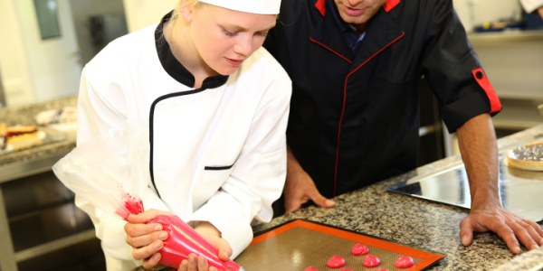 Young female culinary student being guided by teacher to make macarons 