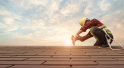 Roof worker wearing safety gear using nail gun to fix shingles to a new roof  