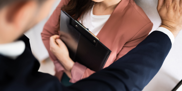 Woman in business suit holding black clipboard cornered by male colleague