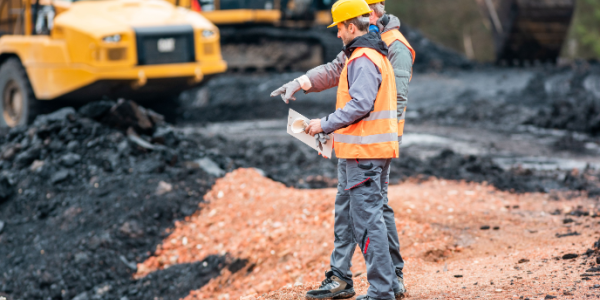 Two workers wearing safety vests and helmets survey an outdoor mining operation.