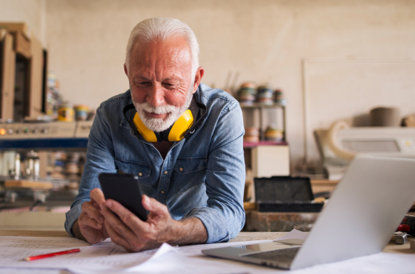 An older worker looks at his phone in a workshop