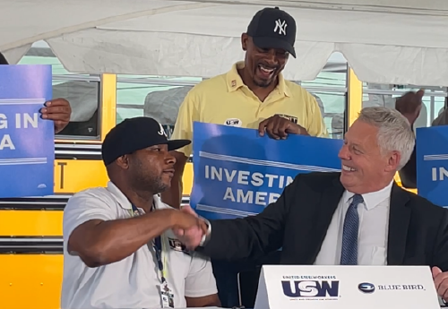 A Blue Bird manager and union representative shake hands at a signing ceremony.