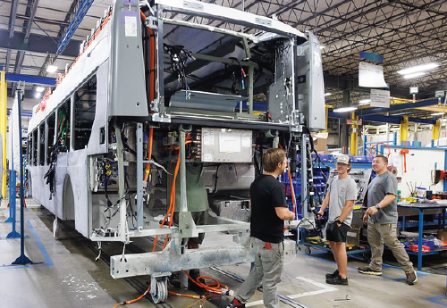 Four people walk through a warehouse where electric buses are under construction.