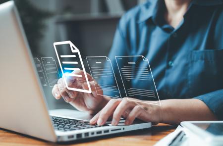 Person typing on a laptop. Translucent document icons float above the keyboard.